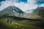 2 people walking on green grass field near snow covered mountain during daytime